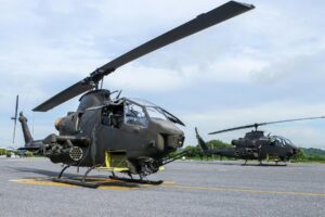 Two military helicopters parked on an outdoor runway on a clear day.
